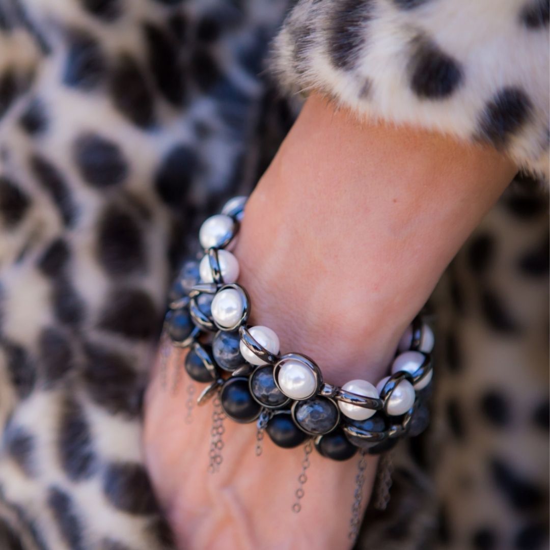 A close-up of a wrist wearing a black and white gemstone bracelet by Brett Lauren, paired with a leopard print coat for a stylish, bold look.