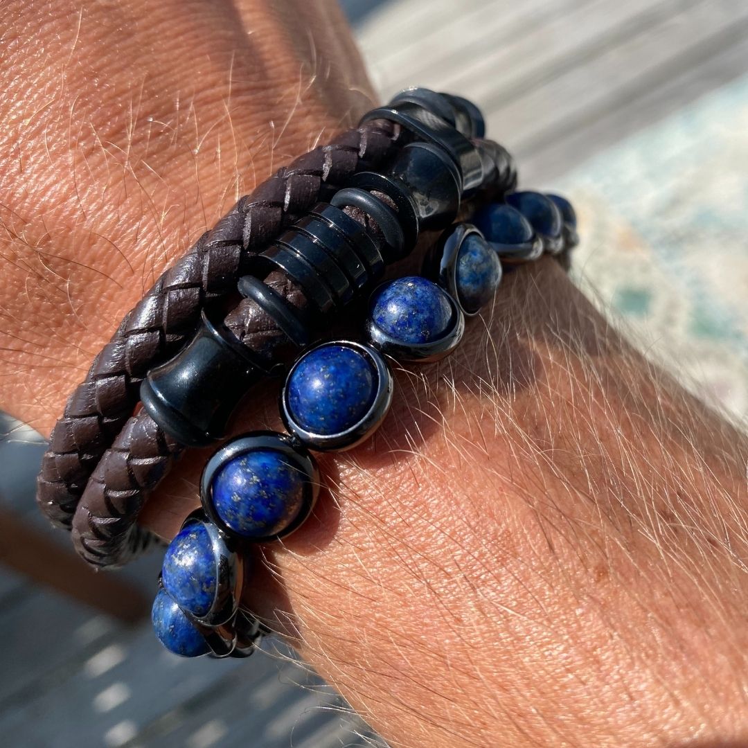 A close-up of a wrist wearing a blue gemstone and leather wrap bracelet by Brett Lauren, photographed outdoors.