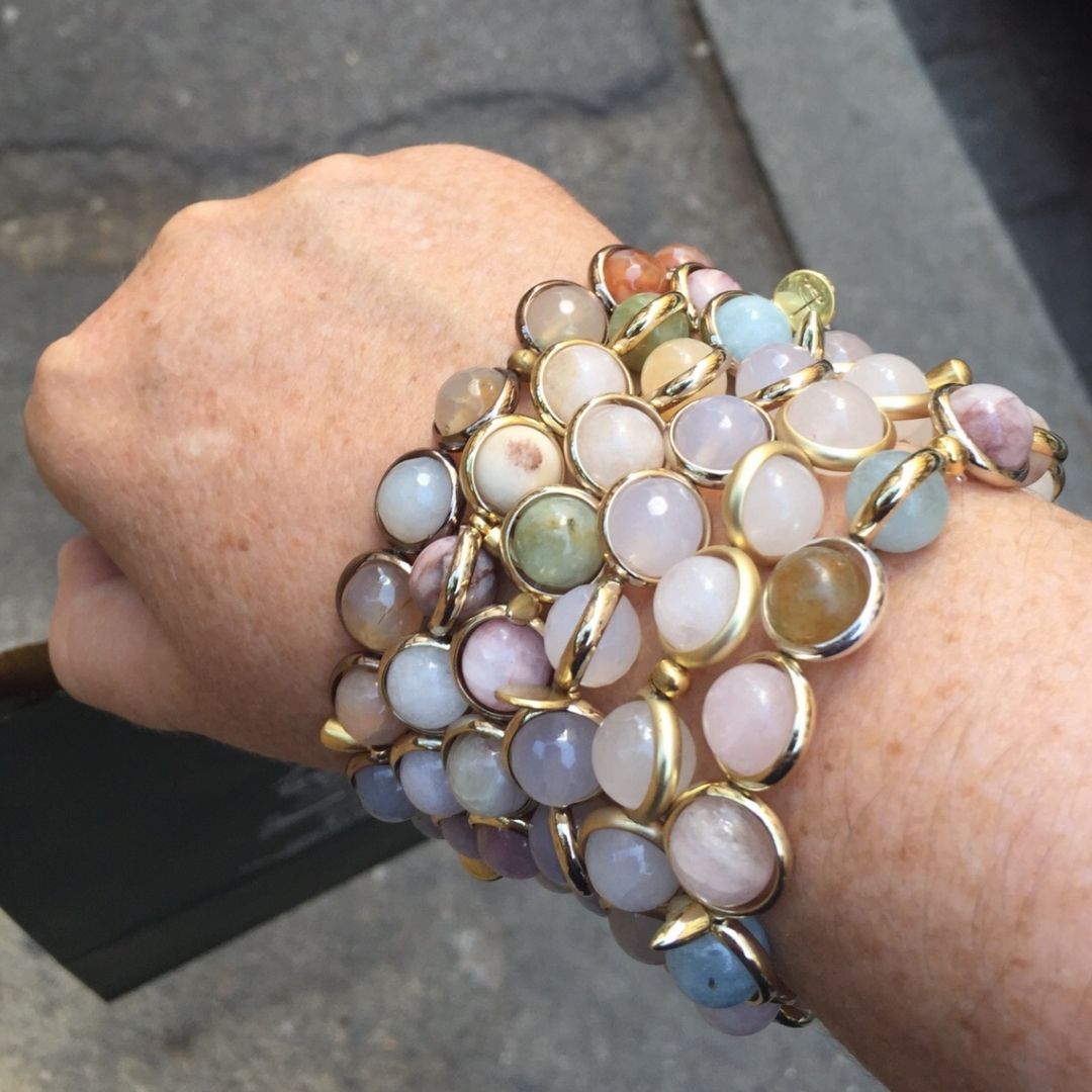 A close-up of a wrist wearing stacked Brett Lauren gemstone bracelets, showing the bracelets in an outdoor setting.