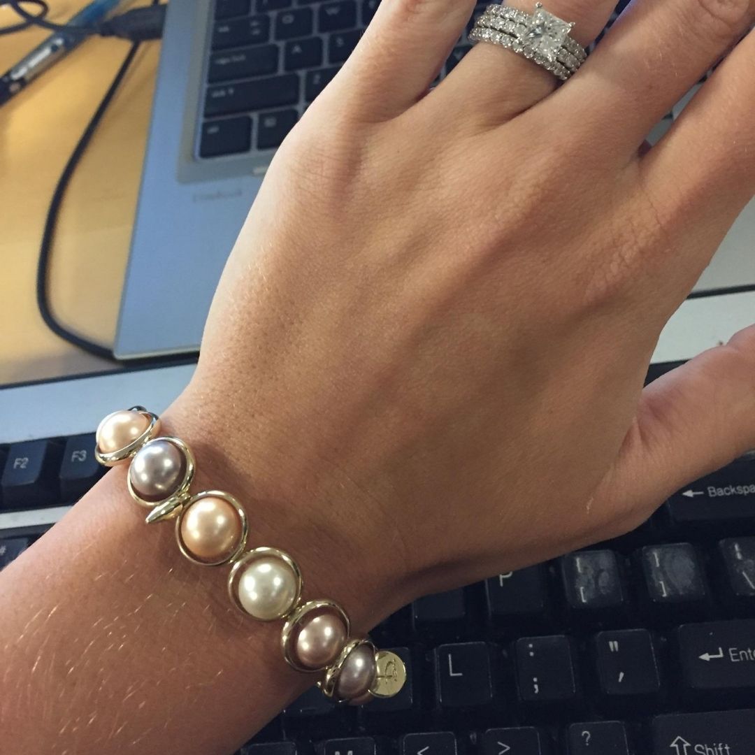 A close-up of a wrist wearing a Brett Lauren pearl gemstone bracelet, photographed in a work setting at a desk with a laptop.