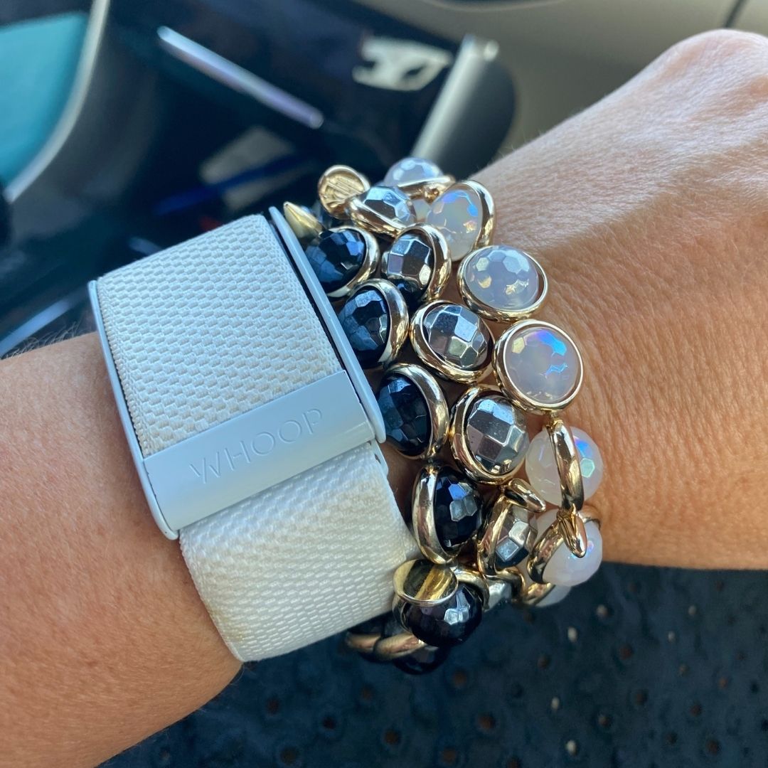 A close-up of a wrist wearing stacked gold and white gemstone bracelets by Brett Lauren, styled alongside a smartwatch for a modern look.