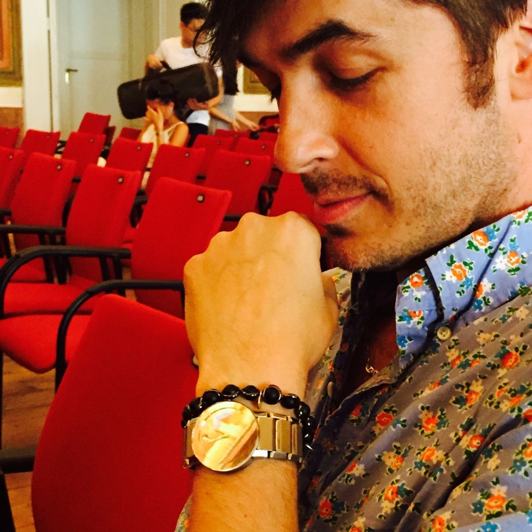 A man wearing a Brett Lauren gemstone bracelet paired with a watch, resting his chin on his hand in a thoughtful pose in a casual setting.