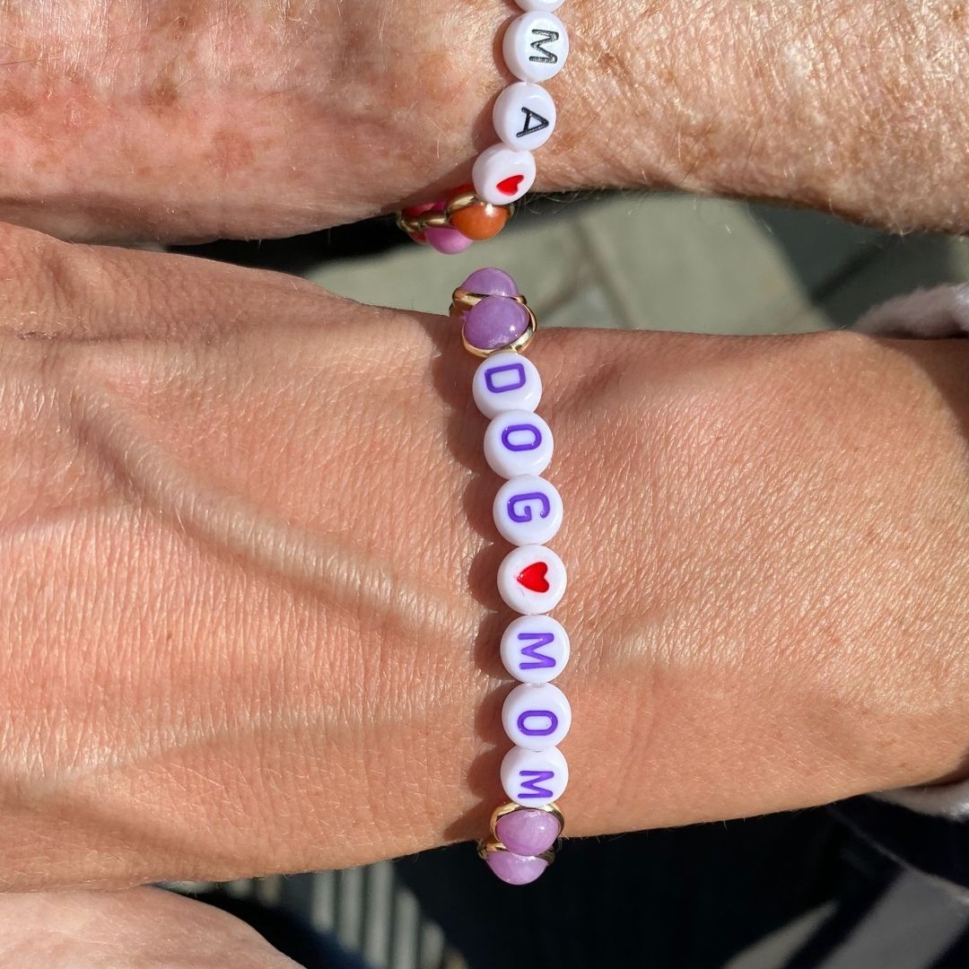 Two wrists wearing matching personalized beaded bracelets with colorful letters by Brett Lauren, showcasing a meaningful design.