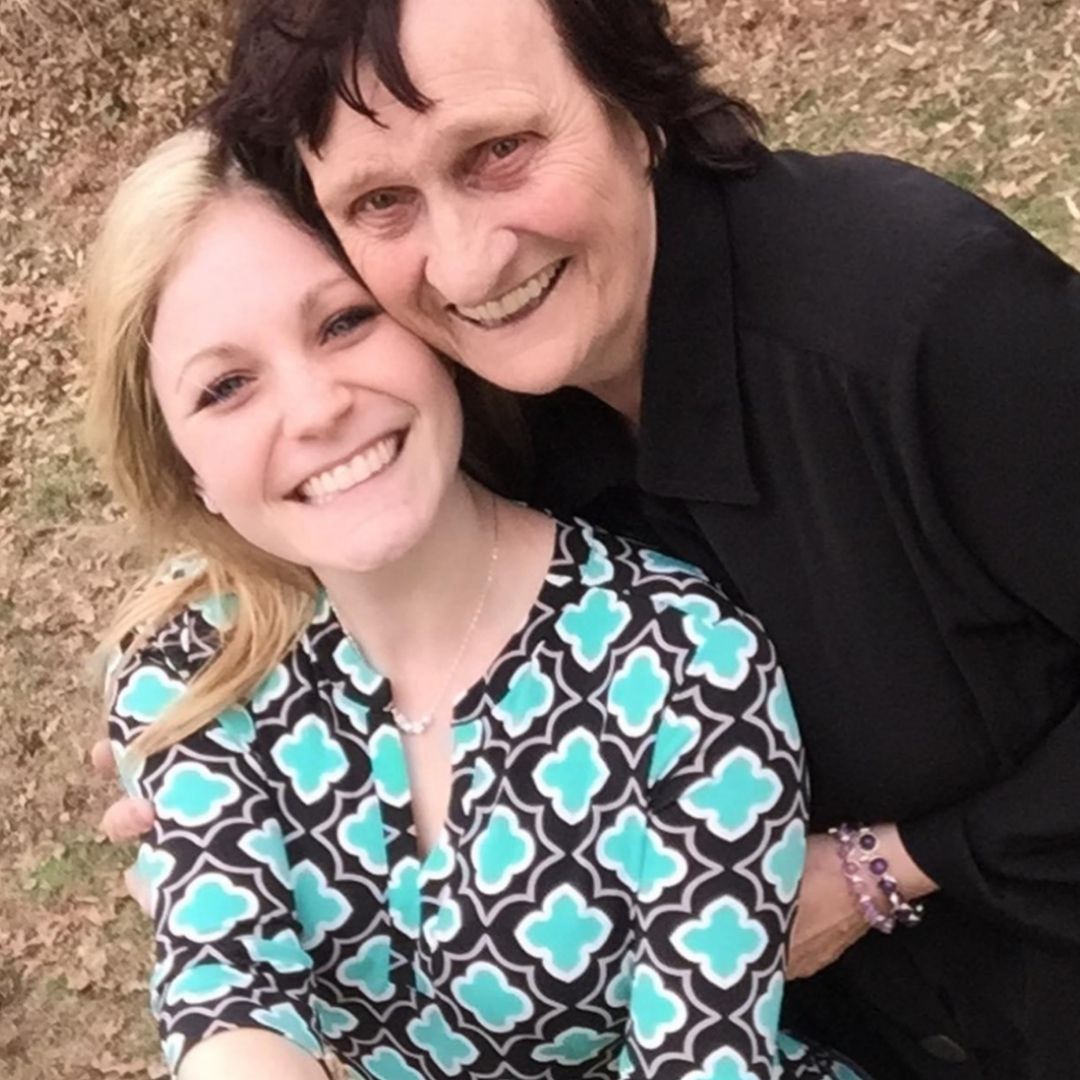 A mother and daughter smiling and embracing, with the daughter wearing a Brett Lauren gemstone bracelet, posed outdoors.