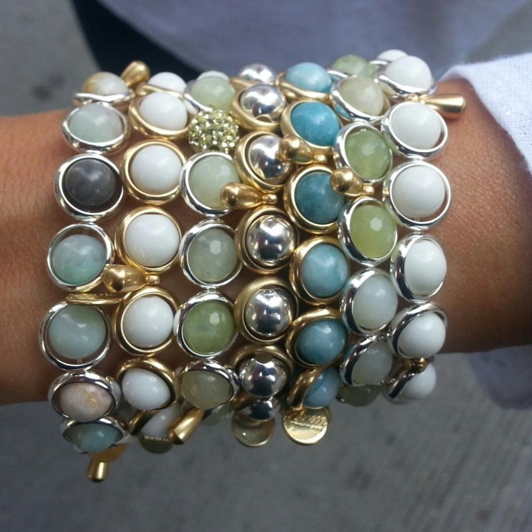 A close-up of a wrist wearing multi-layered gemstone bracelets by Brett Lauren, featuring white and blue stones, photographed in an outdoor setting.