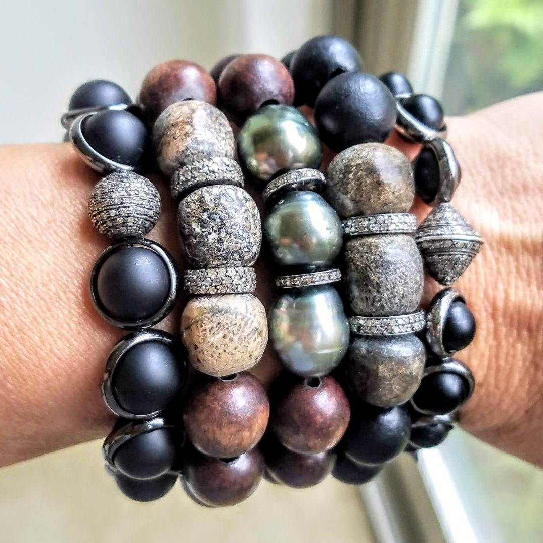 A close-up of a wrist adorned with stacked black and silver gemstone bracelets by Brett Lauren, featuring bold, textured designs.