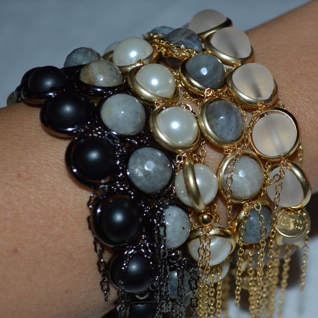 A close-up of a wrist adorned with stacked black, white, and gold gemstone bracelets by Brett Lauren, featuring tassels for a bold and stylish look.