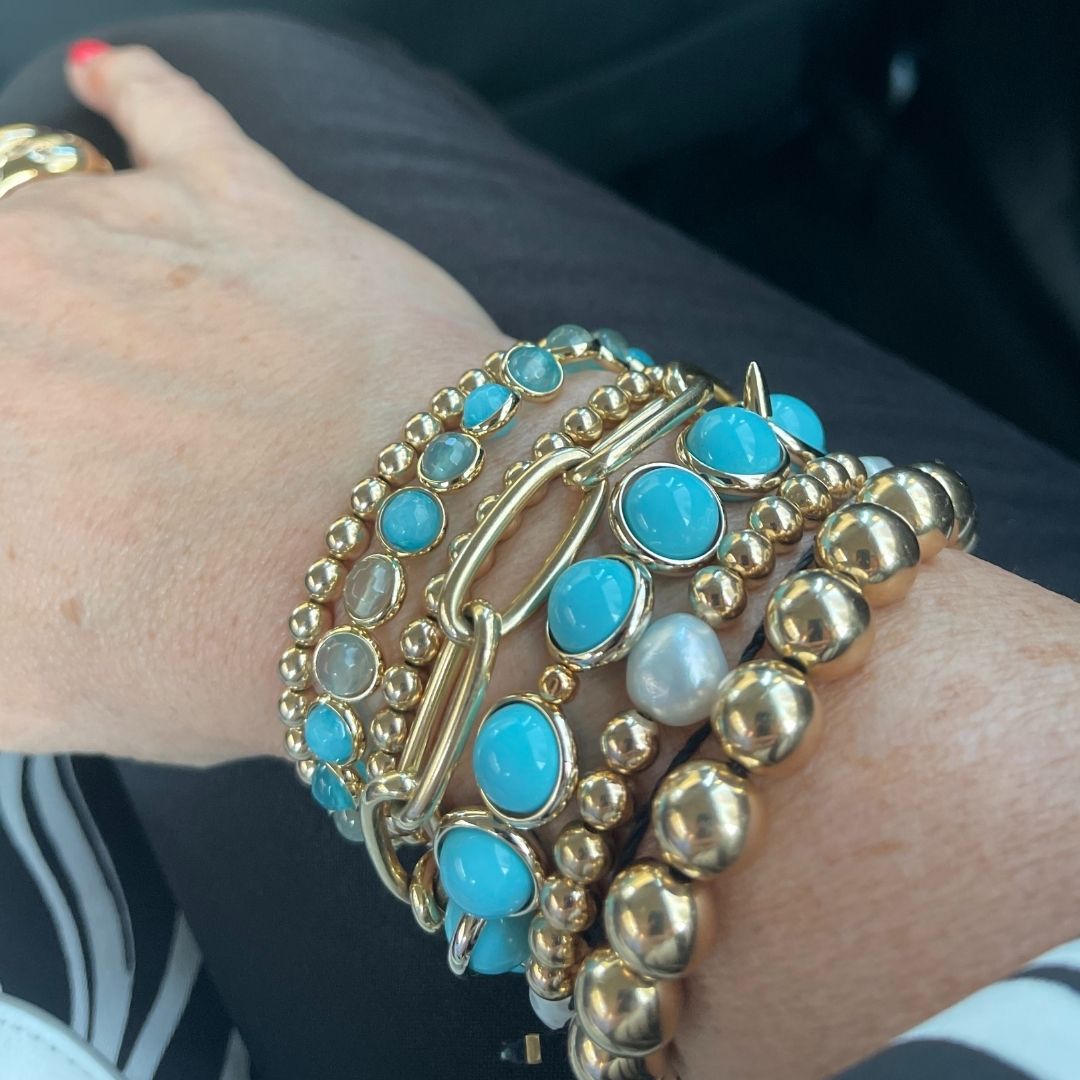 A close-up of a wrist adorned with stacked blue and gold gemstone bracelets by Brett Lauren, photographed inside a car.