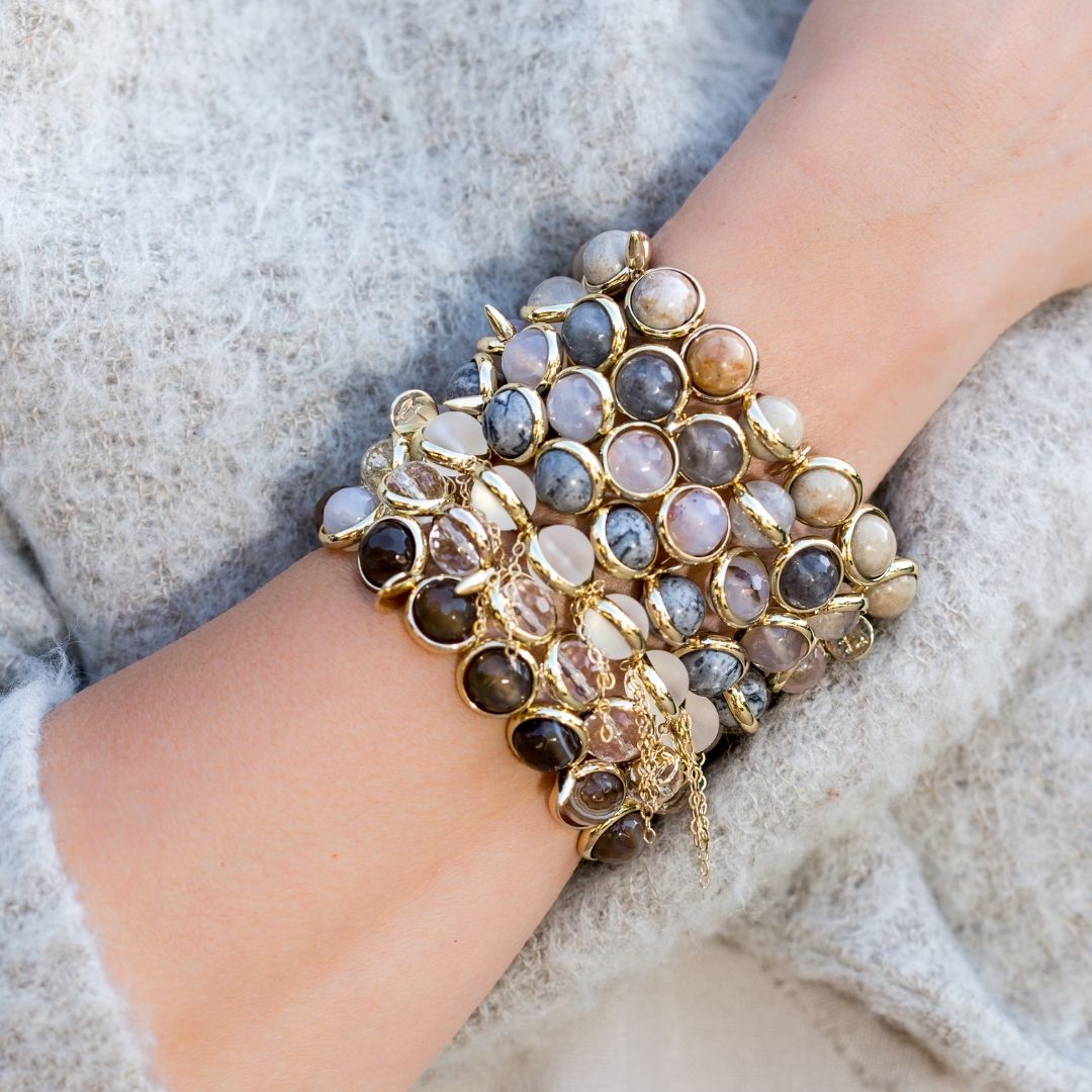 A wrist adorned with stacked gemstone bracelets featuring gold and black tones by Brett Lauren, styled in a cozy sweater.