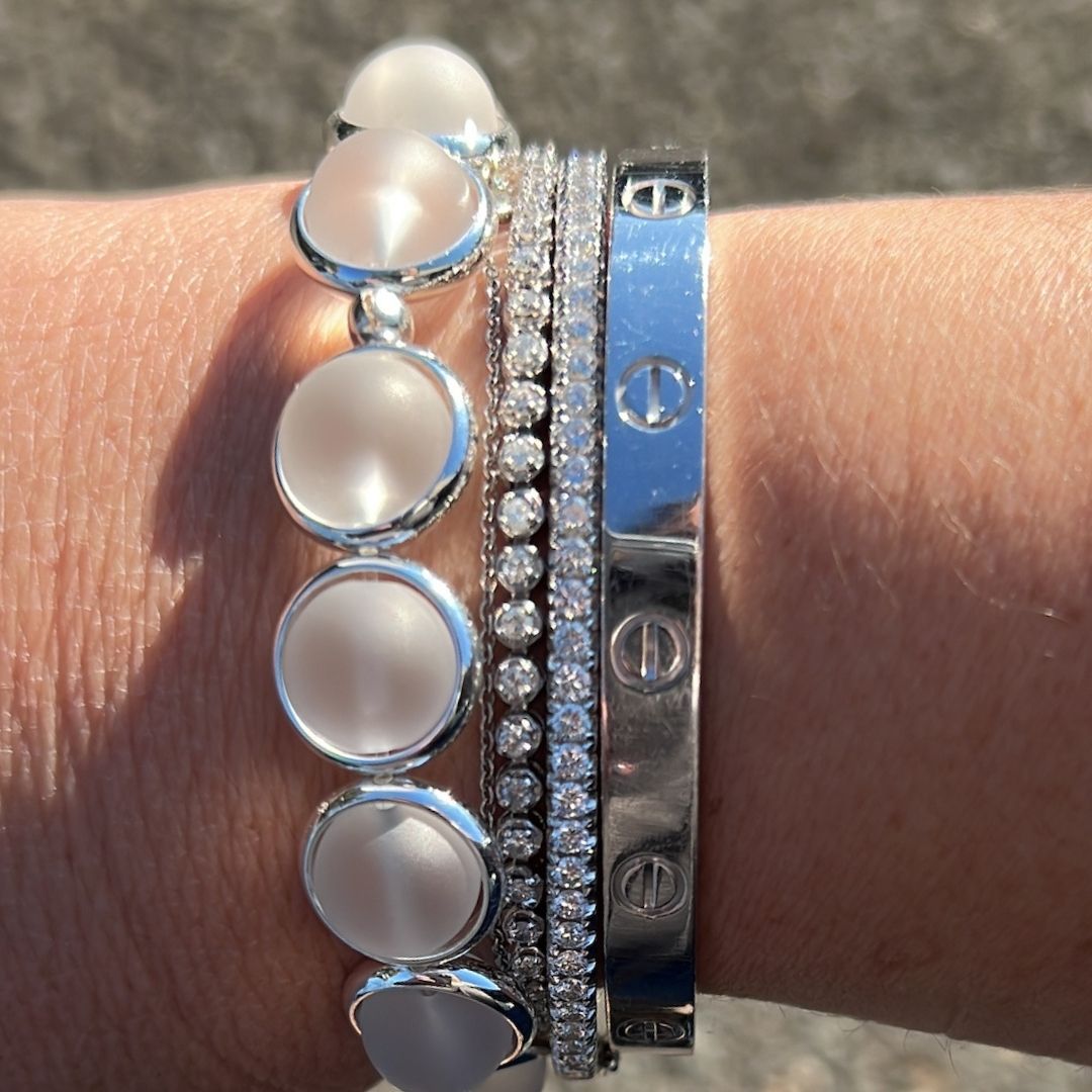 A close-up of a wrist wearing stacked pearl and blue gemstone bracelets by Brett Lauren, photographed in an outdoor setting.