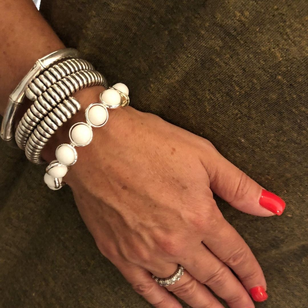 A close-up of a wrist adorned with stacked pearl and silver bracelets by Brett Lauren, styled with red nails and a casual outfit.