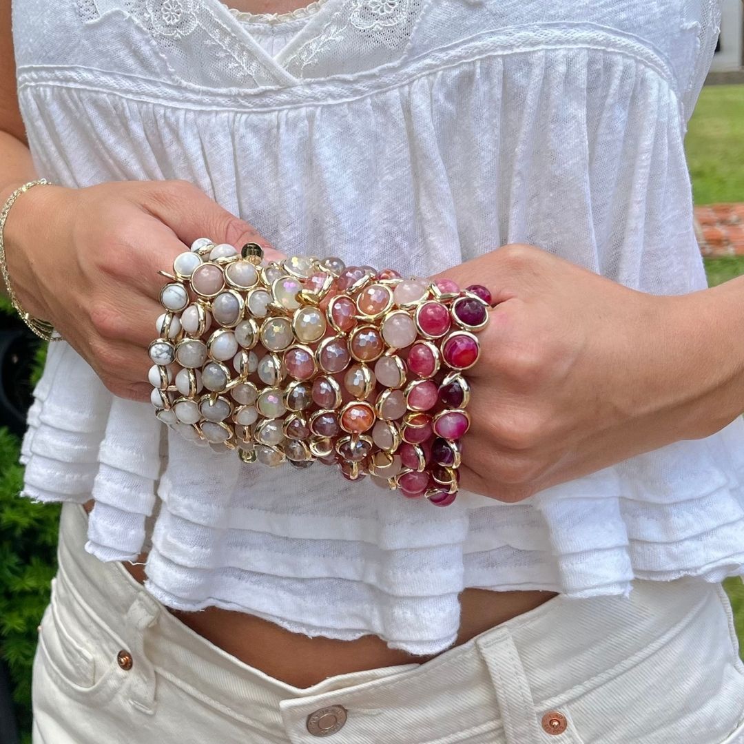 A woman wearing stacked pink and gold gemstone bracelets by Brett Lauren, paired with a casual summer outfit featuring a white top and jeans.