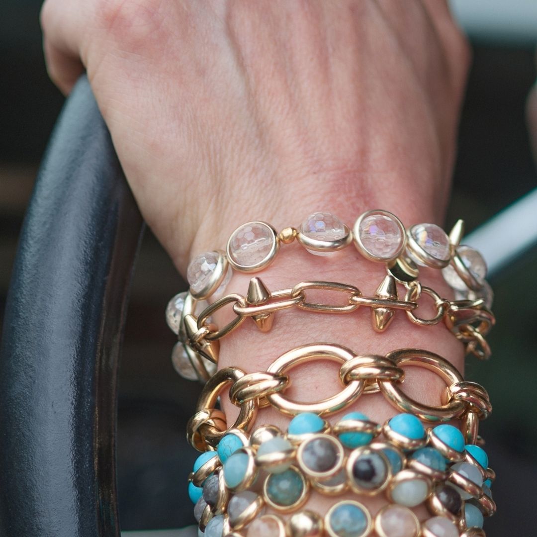 A close-up of a wrist adorned with stacked pink, blue, and gold gemstone bracelets by Brett Lauren while driving.