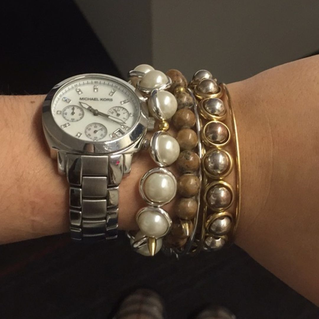 A wrist adorned with a silver watch and stacked Brett Lauren gemstone bracelets featuring gold and white stones, creating a mix of casual and elegant style.