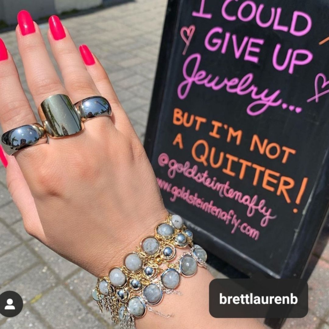 A woman wearing Brett Lauren gemstone bracelets and bold rings, posing with a colorful sign about jewelry, showing off her stylish accessories.