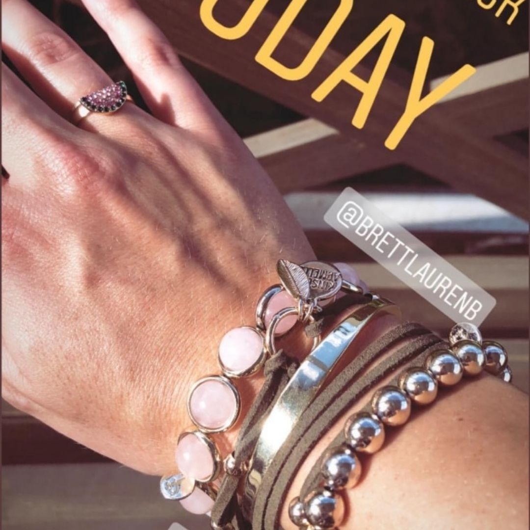 A woman's wrist adorned with stacked pink and pearl gemstone bracelets by Brett Lauren, styled alongside bold rings in an outdoor setting.